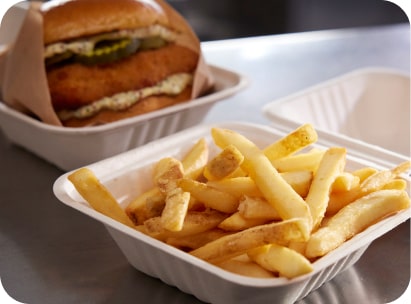 Gros plan de frites McCain® SureCrisp® avec un sandwich au poulet croustillant dans des boîtes à emporter.