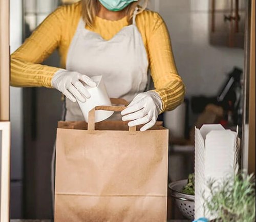 A woman wearing a mask and packing a grocery bag.