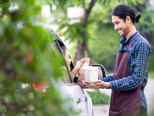 An employee delivering coffee and food to a customer in a parked car.
