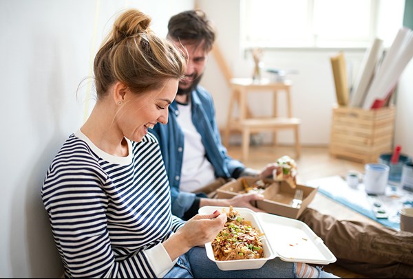 A couple taking a break from painting a room to eat takeout food.